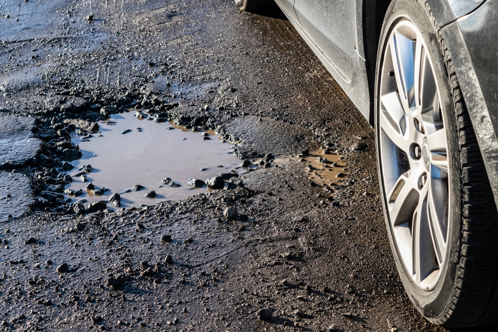Mild Winter Commercial Asphalt Lot Tips for Southern Homeowners 7 Car wheel close-up near a pothole on the broken road.
